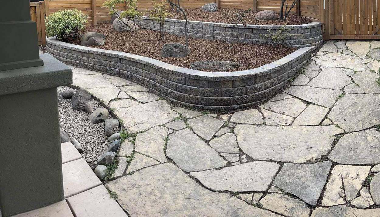 Curved segmental retaining wall, cedar privacy fence, boulder landscaping and flagstone patio built by Gravelle Construction