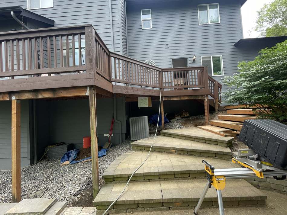 Old brown wood deck and railing before rebuild, with new paver patio steps being installed below