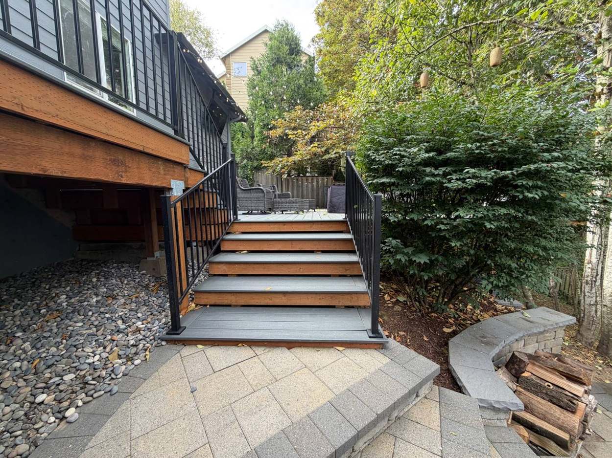 Finished lower deck stairs with black metal railing leading down to paver patio and fire pit area